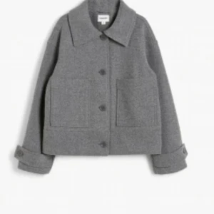 Grå ulljacka med knappar - Fin grå jacka i ull med stora knappar och två framfickor. Jackan har en klassisk krage och långa ärmar med uppvikta muddar. Perfekt för kyligare dagar och ger en stilren look och är andast använd två -tre gånger💕