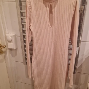 Beige ribbad klänning från Bikbok. - Säljer en stilren beige ribbad klänning med lång ärm och en snygg öppning vid halsen. Perfekt för en chic och bekväm look. Passar bra till både vardag och speciella tillfällen. Den är i stl. S.