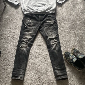 Svarta slitna jeans - Säljer ett par svarta jeans med slitningar och distressed detaljer. De har den trendiga slim passform och är perfekta för en avslappnad stil. Jeansen har klassiska fem fickor och knappgylf. Och passar någon från 175-190