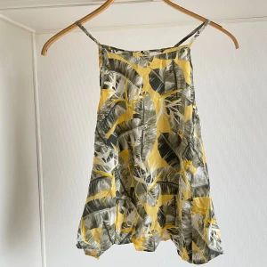 Mönstrad topp från Gina Tricot storlek 40 nyskick  - Snygg topp från Gina Tricot med tropiskt mönster i gult och grönt. Den är ärmlös med smala axelband och har en luftig passform. Perfekt för varma dagar!