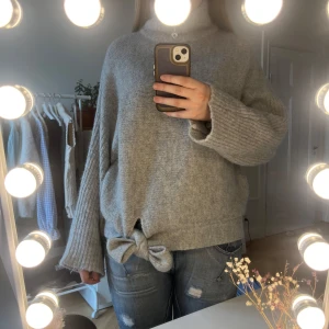 Grå stickad tröja med rosett från Selected Femme - Mysig grå stickad tröja med hög krage (som går att vika ner som på 3:e bilden) och knytning i nederkant🎀Väldigt fin och skön, fått många komplimanger med den! 