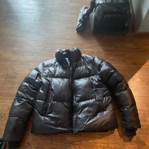Svart pufferjacka från 8848 Altitude - Säljer en svart pufferjacka från 8848 Altitude. Jackan har en hög krage och dragkedja framtill. Perfekt för kalla dagar med sin vadderade design. Den har långa ärmar och en stilren look.