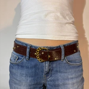 Brunt skärp med gulddetaljer - Snyggt brunt skärp i skinn med guldfärgad kedjedetalj och nitar. Perfekt för att ge en extra touch till din outfit. Passar bra med jeans för en stilren look. 💞