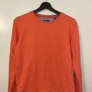 Orange tröja från GANT - Säljer en snygg orange tröja från GANT. Tröjan har en rund halsringning och långa ärmar. Perfekt för en färgglad stil. Passar för ungdomar med storlek 176 cm. !Tröjan är lite ljusare i verkligheten, inte lika orange!