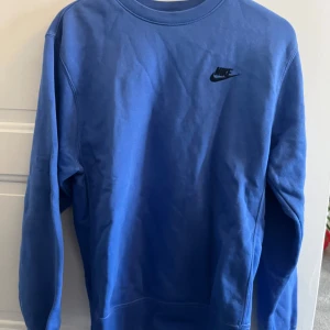 Blå sweatshirt från Nike - Säljer en blå sweatshirt från Nike med rund hals och långärmade design. Tröjan har en enkel och stilren look med Nike-loggan i svart på bröstet. Perfekt för en avslappnad stil.