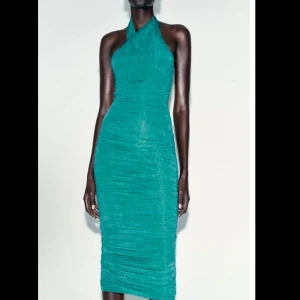 Grön halterneck klänning - Snygg grön halterneck klänning med rynkade detaljer och en tight passform. Klänningen har en elegant längd och en öppen rygg som ger en stilren look. Perfekt för speciella tillfällen.