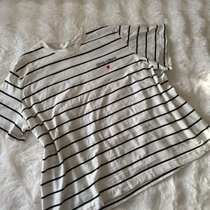 Vit och svart randig t-shirt från H&M - Vit och svart randig t-shirt från H&M med texten 'Live a little' och ett rött hjärta på bröstet.💕 T-shirten har korta ärmar och en klassisk rund halsringning. Perfekt för en avslappnad stil.💕 Passformen är rak till oversized💕 storlek xl💕