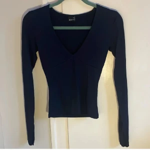 Mörkblå långärmad topp från Gina Tricot - Säljer en stilren mörkblå topp från Gina Tricot med v-ringning. Toppen har långa ärmar och en figurnära passform, perfekt för en trendig look. Passar bra till både jeans och kjol. Ej fri frakt, kostnad för frakt: 50 kr. Pris inklusive frakt 249