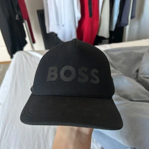 Svart keps från Boss - Snygg svart keps från Boss med justerbar rem baktill. Kepsen har en stilren design med Boss-loggan i svart framtill. Perfekt för en casual look.