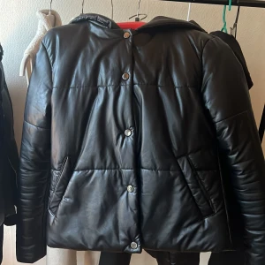 Svart pufferjacka från Boohoo - Säljer en svart pufferjacka från Boohoo i storlek XS. Jackan har en huva och stängs med knappar. Perfekt för kyligare dagar med sin quiltade design och långa ärmar.