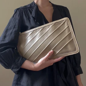 Vintage Anne Klein Leather Clutch with Strap - Vintage Anne Klein Beige Leather Clutch Bag. Brass Metal Zip Enclosure. Interior Zip Pocket. Diagonal Frontal Stitching. Embossed Classic Lion Anne Klein Logo on back of bag.  Detachable Leather Wrist Strap .Small Color Fade Mark on Backside. Small imperfections are not attributed to a design flaw but to the uniqueness and quality of the product, please appreciate them for their character. Very Good Condition.  20 CM/ 7.9 IN Length 35 CM/ 13.8 IN Width 6 CM/ 2.4 IN Depth 18.5 cm/ 7.2 IN Strap