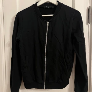 Svart kofta med dragkedja - Snygg svart kofta med dragkedja framtill. Koftan har långa ärmar och ribbade muddar vid ärmslut och nederkant. Perfekt för en stilren look. Storlek 170 men passar xxs-s