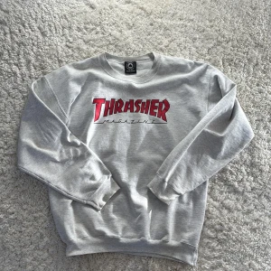 Grå sweatshirt från Thrasher - Säljer en grå sweatshirt från Thrasher med det ikoniska logotyptrycket på framsidan. Tröjan är tillverkad i en mjuk bomullsblandning och har långa ärmar med ribbade muddar. Perfekt för en avslappnad stil. Använd en del men har fortfarande fint skick.