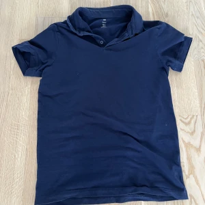 Mörkblå pikétröja från H&M - Säljer en mörkblå pikétröja från H&M i slim fit. Tröjan har korta ärmar och en klassisk krage med knappar.