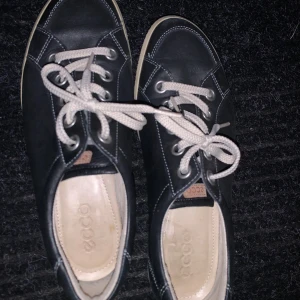 Svarta sneakers från Ecco - Snygga svarta sneakers från Ecco med vita snören och kontrasterande sömmar. Perfekta för en avslappnad stil. Skorna har en klassisk design med rund tå och bekväm passform.
