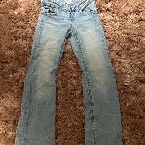Ljusblå jeans från Gina Tricot - Säljer syrrans jeans. Snygga ljusblå jeans från Gina Tricot med en klassisk femficksdesign. Byxorna har en rak passform och är perfekta för en avslappnad stil. De har dekorativa ficklock på bakfickorna som ger en extra detalj. Fina jeans, men har tyvärr en gräs fläck vid vänster knäskål (se bilder)