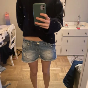 Blå jeansshorts med slitningar - Snygga blå jeansshorts med slitna detaljer och fransig kant. De har fem fickor och en knappgylf. Perfekta för en avslappnad stil.