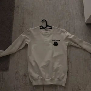 Vit tröja från Palm Angels x Moncler - Säljer en stilren vit tröja från Palm Angels i samarbete med Moncler. Tröjan har en broderad logga på bröstet och är tillverkad i ett mjukt material. Perfekt för en avslappnad look.