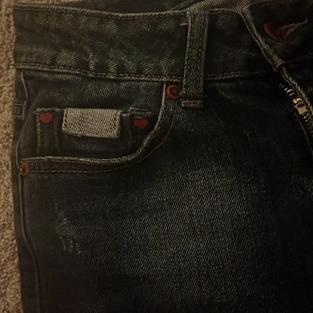 Snygga svarta bootcut jeans med färgglatt blommigt broderi på ena benet. Jeansen har en klassisk femficksdesign och är tillverkade i ett robust denimtyg. Perfekta för att ge din outfit en unik touch.. Farkut & Housut.