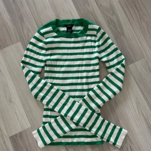 Grön och vit randig tröja från Lindex - Säljer en snygg grön och vit randig tröja från Lindex. Tröjan är ribbad och har långa ärmar, perfekt för en stilren look. Passar bra till både jeans och kjol. Hör av dig vid intresse! 💚