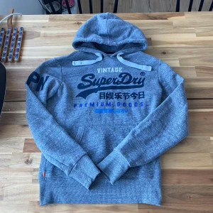 Grå hoodie från SuperDry - Säljer denna feta gråa hoodie från Superdry. Riktigt fet hoodie utan defekter och i riktigt fin skick!!! S i storlek men passar även M! Skriv om du har några funderingar😁✅!