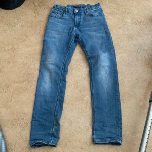 Blå jeans från Tommy Hilfiger - Snygga blå jeans från Tommy Hilfiger med klassisk design. De har en rak passform och är tillverkade i slitstarkt denim. Perfekta för en avslappnad stil. Märkesdetaljer syns på baksidan och insidan av midjan.