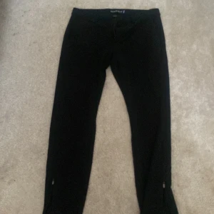 Svarta kostymbyxor från Gabba - Snygga svarta byxor från Gabba med dragkedja och knapp framtill. Perfekta för en stilren look. Byxorna har en klassisk design med midwaist och är tillverkade i ett bekvämt material.