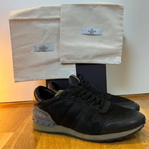  Valentino rockrunners  - Snygga svarta Valentino sneakers med grå och vinröda detaljer. Skorna har en unik design med nitar på sulan och är tillverkade i en kombination av skinn och syntetmaterial. Perfekta för en stilren look. Liten defekt skriv privat för bild