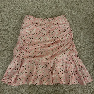 Rosa blommig kjol med volang - Söt rosa kjol med blommigt mönster och volangdetaljer. Perfekt för en somrig look. Kjolen har en kort längd och en smickrande passform. Lånade bilder!! Kjolen är aldrig använd! Fraktar endast varan och köparen betalar frakten! Priset som syns är vad som gäller🙏🫶