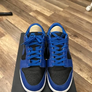 Nike Dunk i blått och svart - Snygga Nike Dunk sneakers i en fräsch kombination av blått och svart. Skorna har en klassisk design med snörning och en bekväm sula. Perfekta för en stilren look.