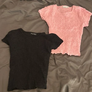 Svart och rosa ribbade toppar - Två ribbade toppar i svart och rosa. Båda har korta ärmar och en texturerad yta som ger en unik look. Perfekta för en avslappnad stil. 250 för båda