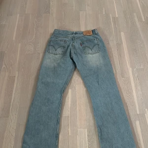 Levis jeans i ljusblå denim - Säljer ett par klassiska Levis jeans i ljusblå denim. De har en straight passform och är midwaist. Perfekta för en avslappnad stil. Jeansens slitna look ger dem en cool vintagekänsla.
