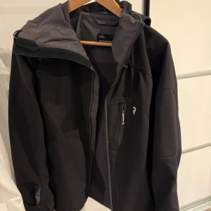 Svart softshelljacka från Peak Performance - Säljer en svart softshelljacka från Peak Performance i mycket bra skick. Jackan har en dragkedja framtill och en praktisk huva. Perfekt för höst och vår med sin stilrena design och funktionella fickor. Passar både till vardags och lättare friluftsaktivitet. Använd som skidjacka 