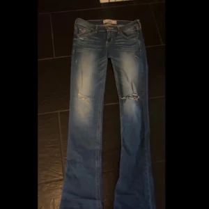 Blå jeans från Hollister - Säljer ett par snygga blå jeans från Hollister i storlek 26. De har slitningar på framsidan för en trendig look. Perfekta för både vardag och fest! 🦋 de passar mig perfekt i längden och jag är 168cm skriv vid frågor ❤️ de passar någon som har xs-s