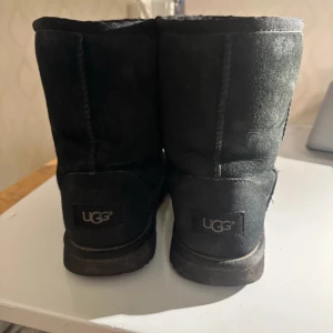 Svarta UGG boots - Säljer ett par svarta UGG boots i bra skick. De är gjorda av mjuk mocka och har en varm insida, perfekt för kalla dagar. Klassisk design med rund tå och låg klack. Passar perfekt till höst- och vinteroutfits.