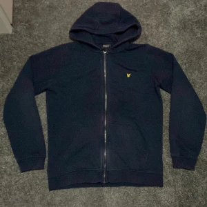 Mörkblå hoodie från Lyle & Scott - Säljer en snygg mörkblå hoodie från Lyle & Scott i storlek 15/16. Den har en dragkedja framtill och en gul broderad logga på bröstet. Perfekt för både vardag och chill. Huvan gör den extra mysig! (Accepterar endast Swish pga lurendrejerier) (Check gärna in kläder från min profil och köp tillsammans för ett rabatterat pris)