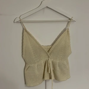 Beige stickad linnetopp - Charmig beige stickad linnetopp med knytning framtill. Toppen har smala axelband och en v-ringad design. Perfekt för varma dagar.