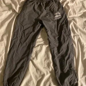 Grå byxor från Corteiz - Säljer ett par grå byxor från Corteiz med elastisk midja och snörning. Sitter som L. Byxorna har en tryckt logga på sidan med texten 'Corteiz Rules The World'. Perfekta för en avslappnad stil.