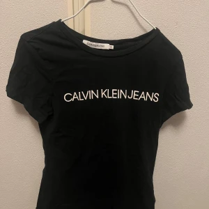 Svart t-shirt från Calvin Klein Jeans - Säljer en snygg svart t-shirt från Calvin Klein Jeans i storlek XS. Den har en klassisk design med korta ärmar och märkesloggan tryckt i vitt på framsidan. 