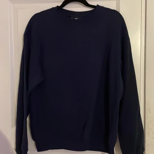 Mörkblå tröja från H&M - Säljer en stilren mörkblå tröja från H&M. Tröjan har en klassisk design med långa ärmar och rund halsringning. Perfekt för en avslappnad look. Storlek S