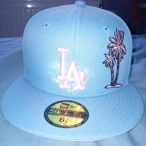 Ljusblå keps från New Era - Säljer en snygg ljusblå keps från New Era med broderad LA-logga och palmer på framsidan. Baksidan har en cool taco-brodyr. Kepsen är i 59FIFTY-modell och passar perfekt för sommaren. Skick 10/10 hel ny