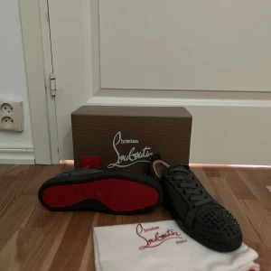 Christian Louboutins - Snygga gråa sneakers från Christian Louboutin med ikoniska röda sulor och nitar på tån. Skorna har snörning och är perfekta för att ge en edgy touch till din stil. Priset ligger på 1599 kr just nu för att vi har vår black friday rea, orginal pris är 2099 kr! Låda medföljer ej!