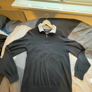 Svart tröja med dragkedja från Dressmann - Säljer en stilren svart tröja från Dressmann i storlek M. Den har en dragkedja framtill och en kontrasterande krage i ljusare färg. Perfekt för både vardag och lite finare tillfällen. Passar bra till höst och vinter passar s också.