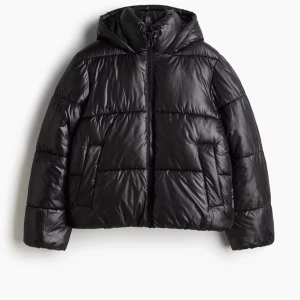 Svart pufferjacka med huva - Snygg svart pufferjacka med huva och dragkedja. Perfekt för kyliga dagar med sin vadderade design. Jackan har långa ärmar och två praktiska fickor framtill.