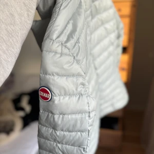 Ljusgrå pufferjacka från Colmar - Snygg ljusgrå pufferjacka från Colmar med quiltad design. Jackan har en stilren look med knappar framtill och en hög krage för extra värme. Perfekt för kyliga dagar.