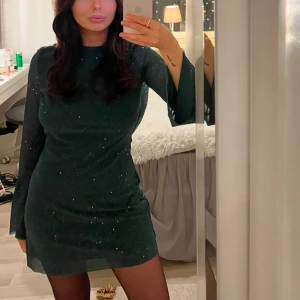 Glittrig mörkgrön klänning - Snygg mörkgrön klänning med glittriga detaljer. Klänningen har långa ärmar och en kort längd, perfekt till nyår, endast använd 1 gång! Öppen rygg 🪩