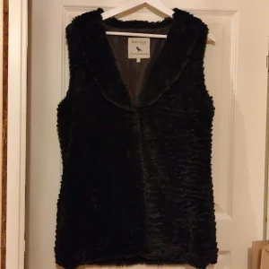 Svart pälsväst från Marc Lauge - Snygg svart pälsväst från Marc Lauge, perfekt för att hålla sig varm och stilren. Västen har en mjuk och fluffig textur som ger en lyxig känsla. Passar utmärkt för kyligare dagar.