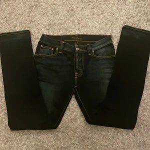Svarta jeans från Nudie Jeans - Snygga mörkblåa jeans från Nudie Jeans med orange sömmar. Jeansen har en normal passform och är tillverkade i denim. Skick 9/10, jag har använt dom 2-3 gånger. Priset är förhandlingsbart, fråga om det är något du undrar!!