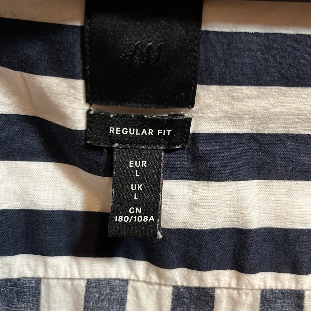 Säljer en snygg randig skjorta från H&M i storlek L. Skjortan är marinblå och vit med korta ärmar och knappar framtill. Regular fit för en bekväm passform. Använd, i bra skick.. Skjortor.