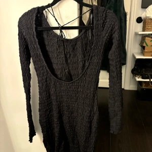 Svart klänning från Pull&Bear - Snygg svart klänning från Pull&Bear med långärmad design och öppen rygg. Klänningen har en unik textur och snörning i ryggen för en stilfull look. Perfekt för en kväll ute eller en speciell tillställning. Aldrig använd med lappen kvar, storlek M💕🙌🙌